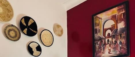A bed with a striped blanket, a red wall with a painting, and wall-mounted woven baskets.