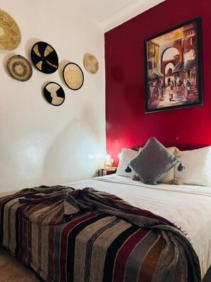 Un lit recouvert d’une couverture à rayures, un mur rouge orné d’un tableau et des paniers tressés accrochés au mur.