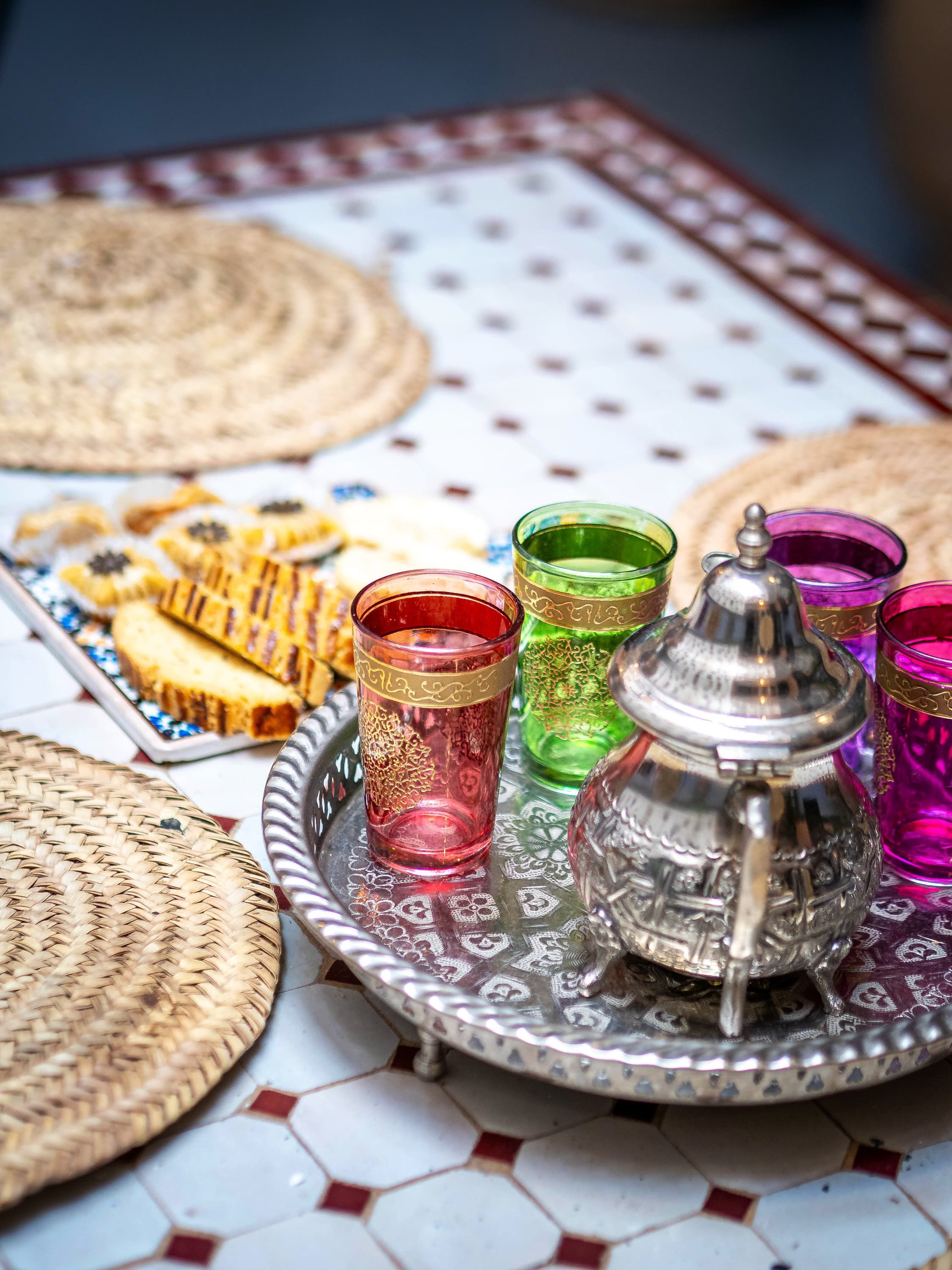 A tray with colorful glasses and a silver container, set on a patterned tablecloth.