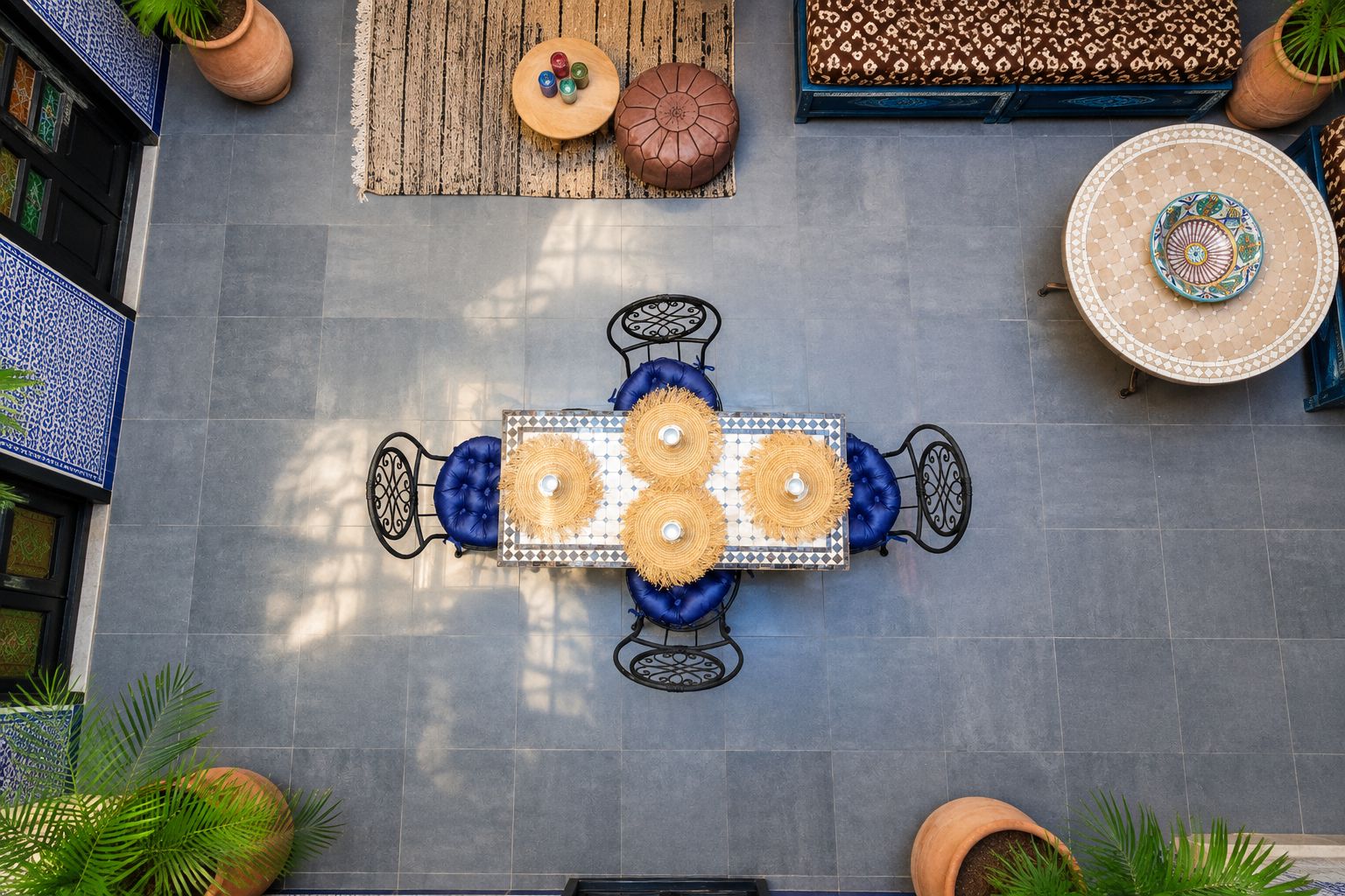 A top-down view of a dining area with a table set for four, surrounded by chairs with blue cushions, and a decorative rug.