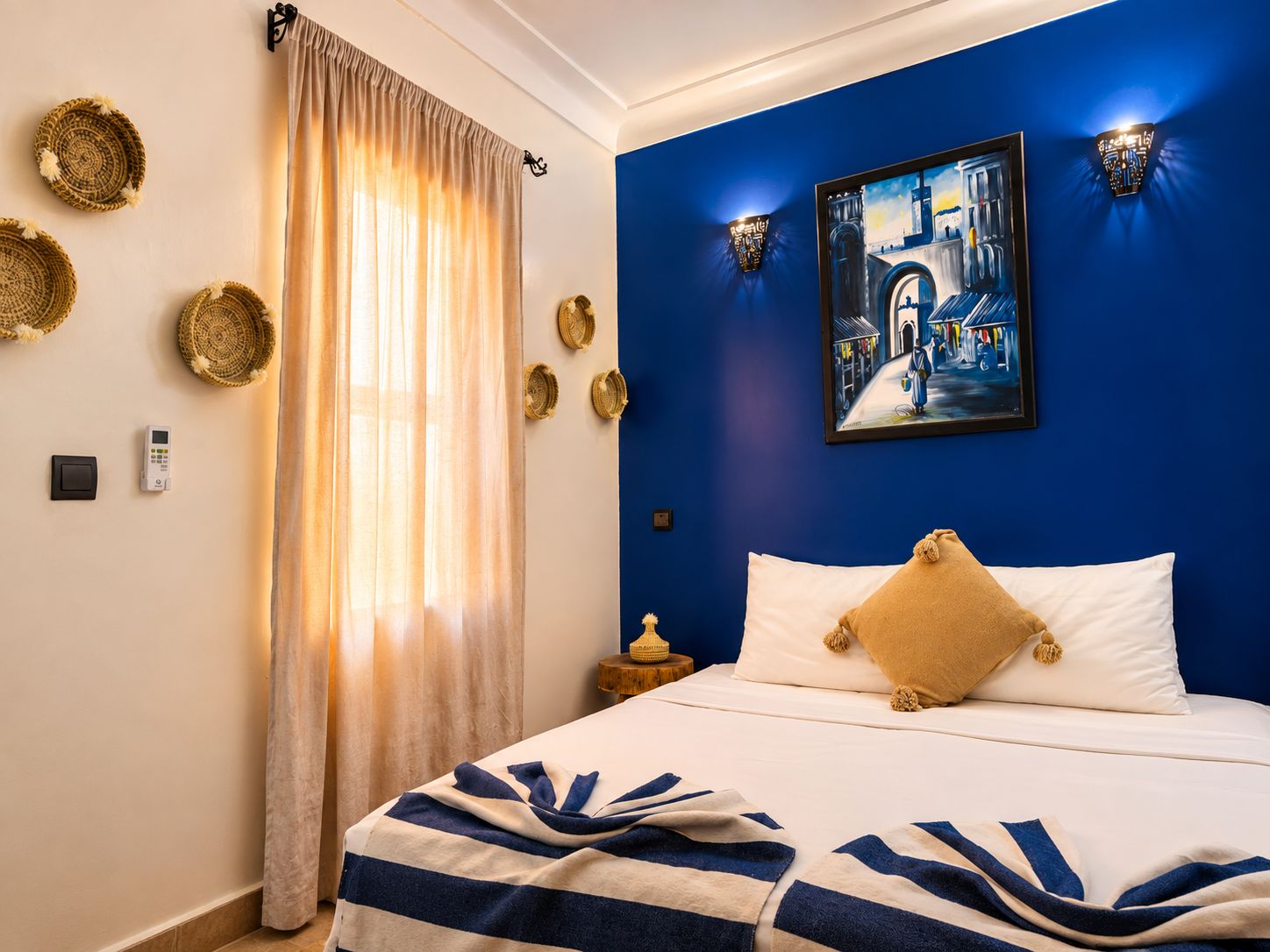 A hotel room with a bed, a painting, a nightstand, and a window with curtains.