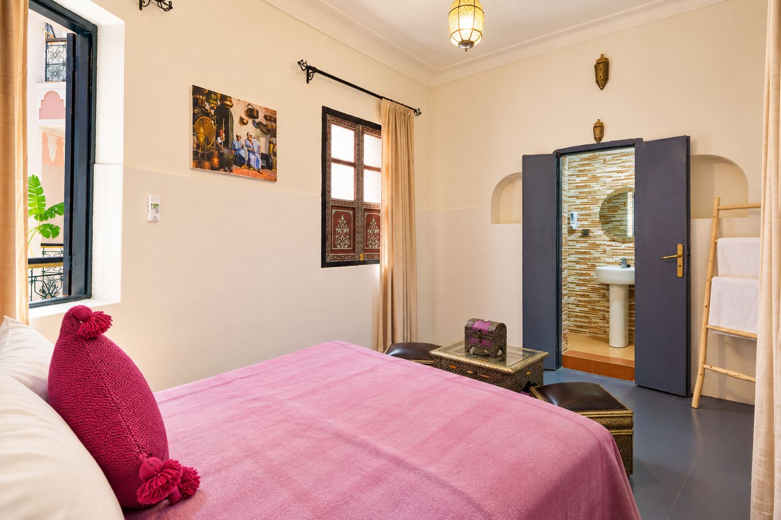 A room with a bed, a small table, a wardrobe, and a bathroom with a sink and mirror.