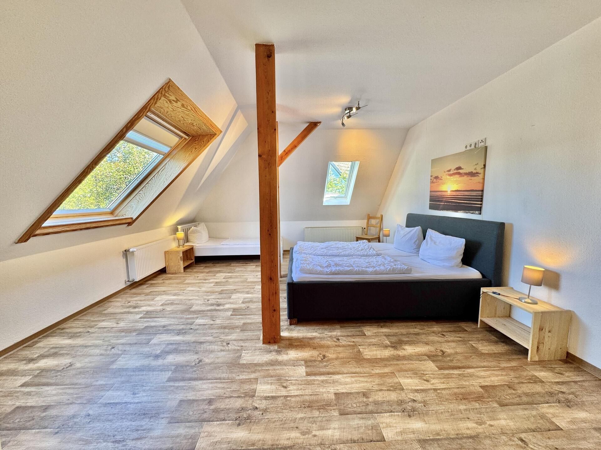 A bedroom with a sloped ceiling, a bed, a wooden floor, and skylights.
