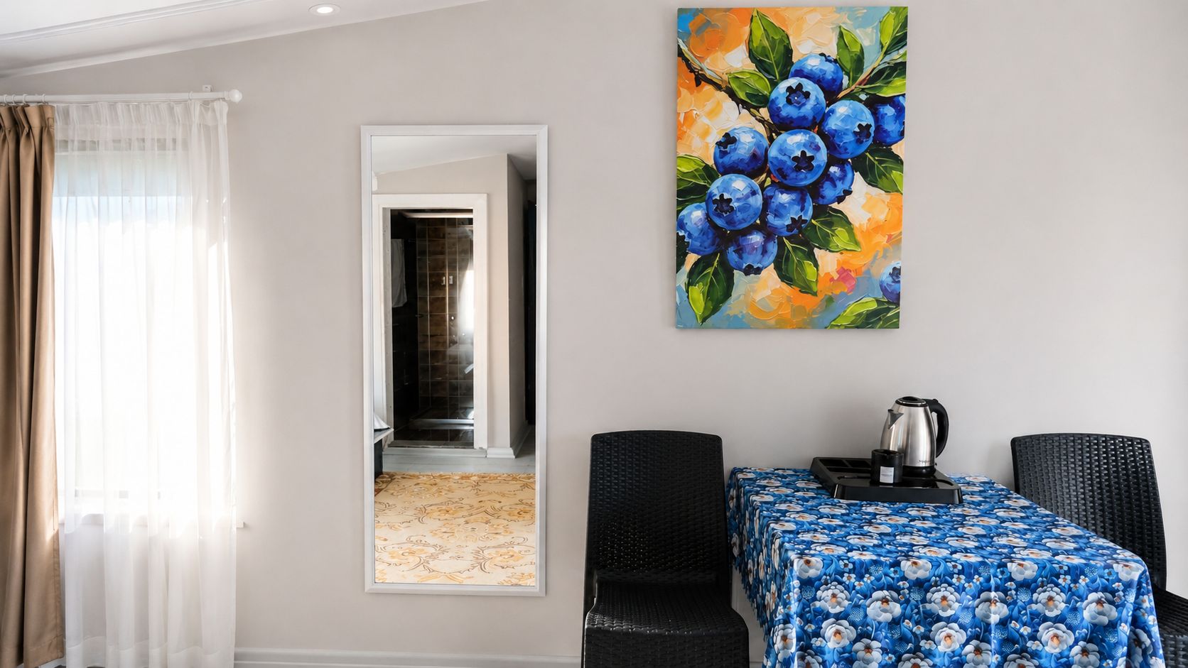 A hotel room with a dining area, a painting of blueberries on the wall, and a view into the hallway.