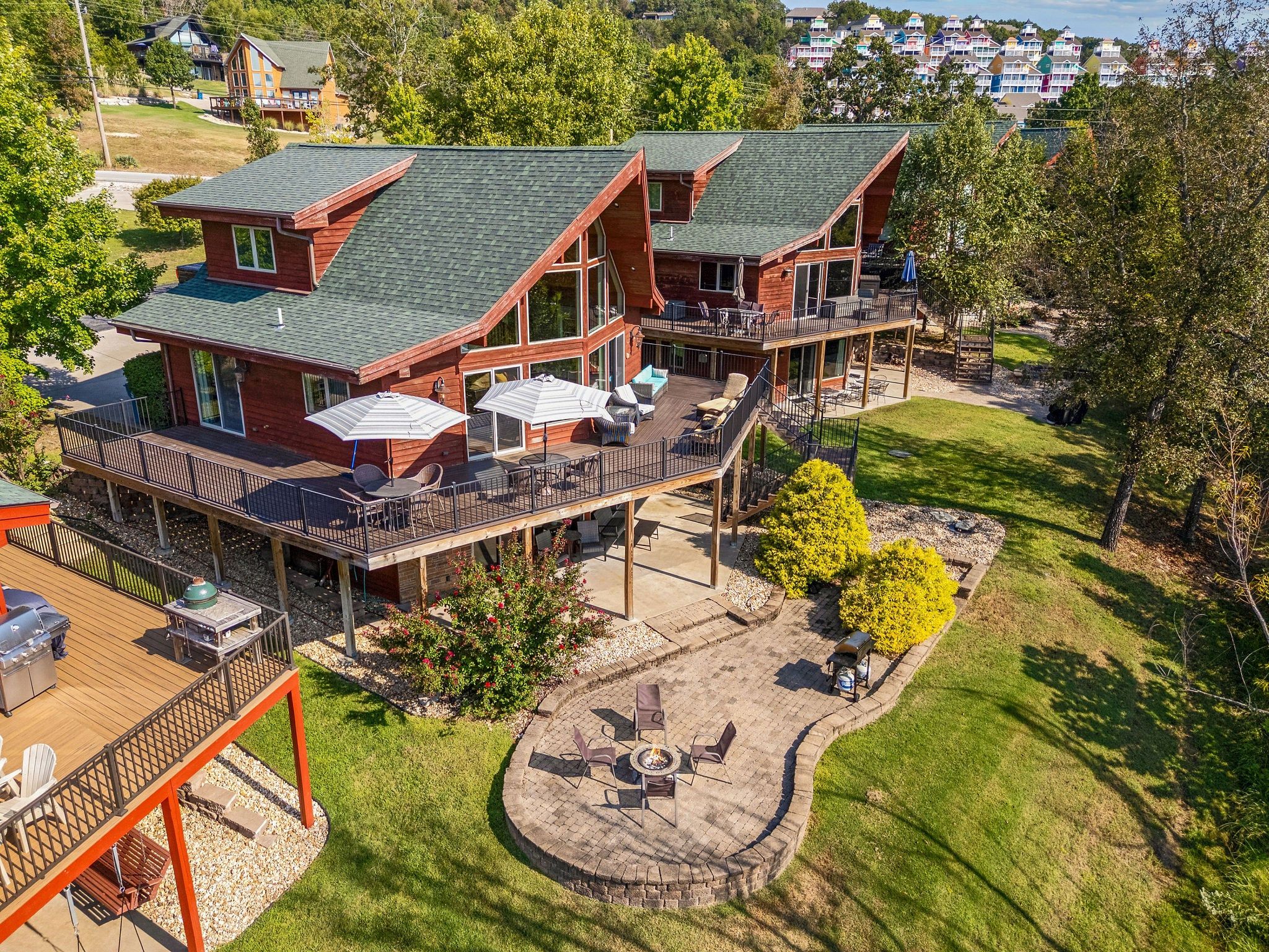 A two-story wooden house with a deck, outdoor seating, and a fire pit.