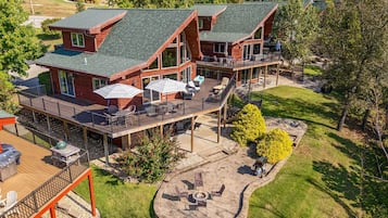 A two-story wooden house with a deck, outdoor seating, and a fire pit.