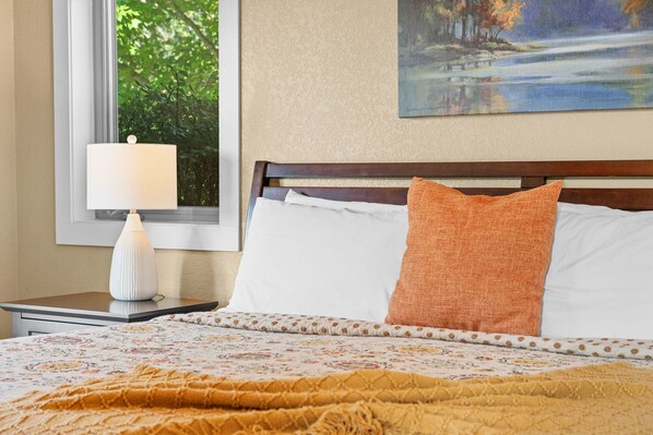 A neatly made bed with a floral-patterned bedspread, a white pillow, and an orange accent pillow.