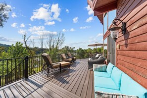 A wooden deck with outdoor furniture, including chairs and a sofa, overlooking a scenic landscape.