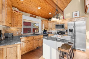 A kitchen with wooden cabinets, a stainless steel refrigerator, a microwave, and a large island with stools. - Walk to Table Rock Lake from your Log Cabin-Free Daily Attraction Tickets (Branson)