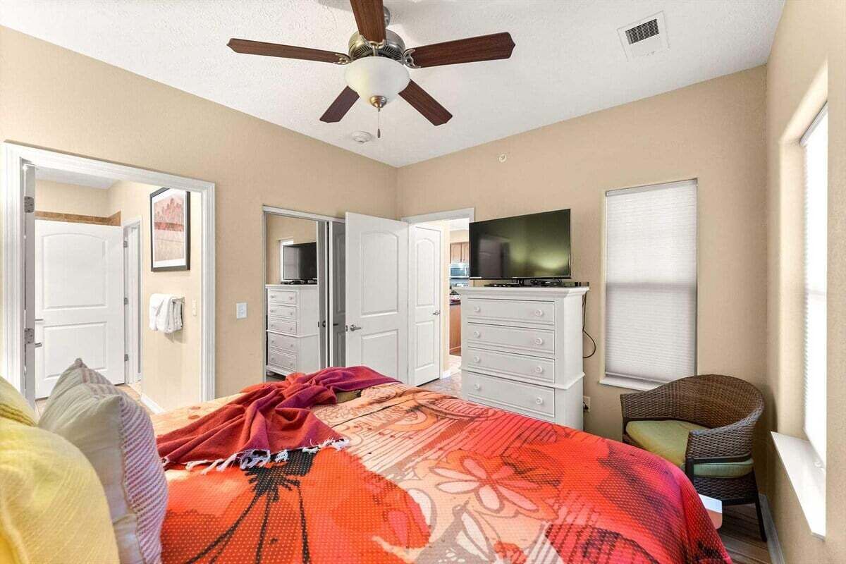 A bedroom with a bed, a television, a ceiling fan, and a chair.