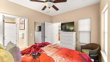 A bedroom with a bed, a television, a ceiling fan, and a chair.