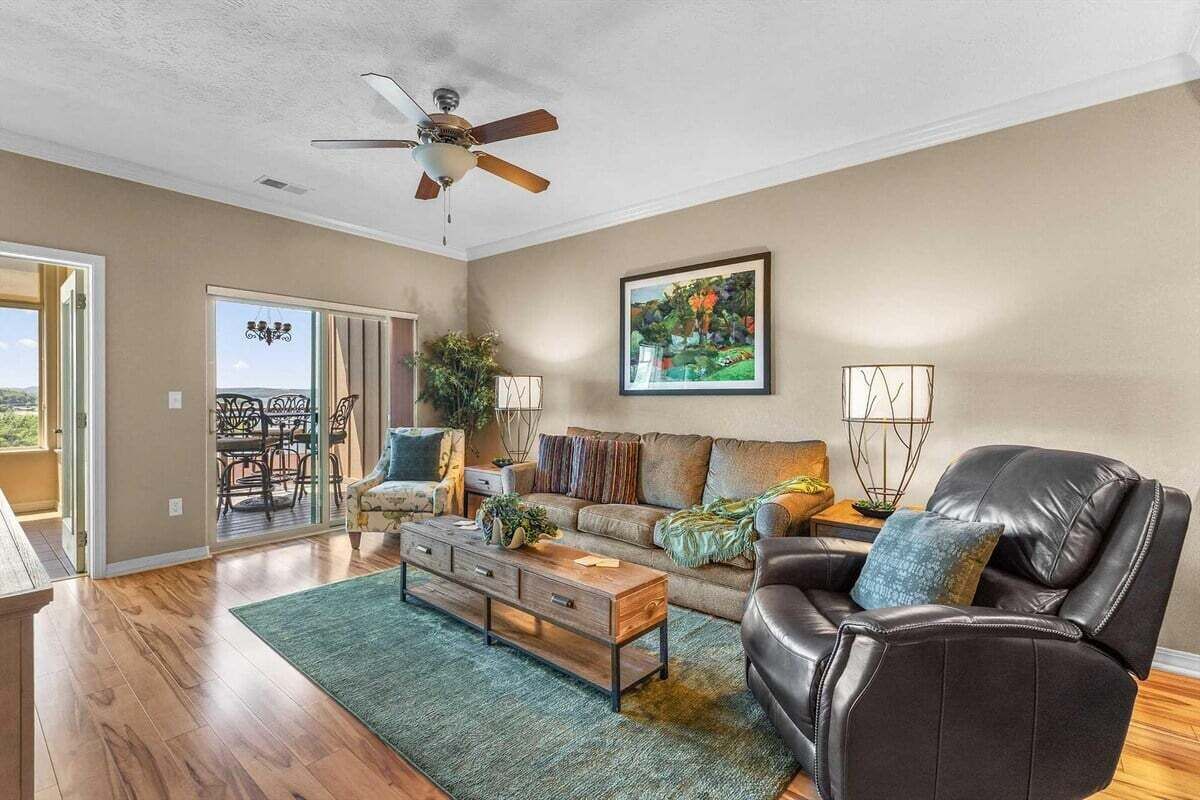 A spacious living room with a ceiling fan, a sofa, a leather chair, a coffee table, and a painting on the wall.