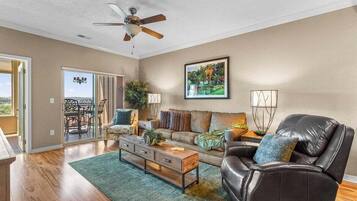 A spacious living room with a ceiling fan, a sofa, a leather chair, a coffee table, and a painting on the wall.