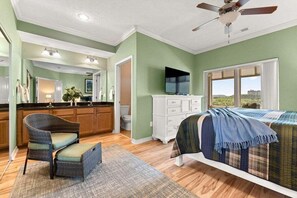 Une chambre avec un lit, un ventilateur de plafond, une fenêtre donnant sur un beau paysage, et une salle de bain avec des toilettes et un lavabo.