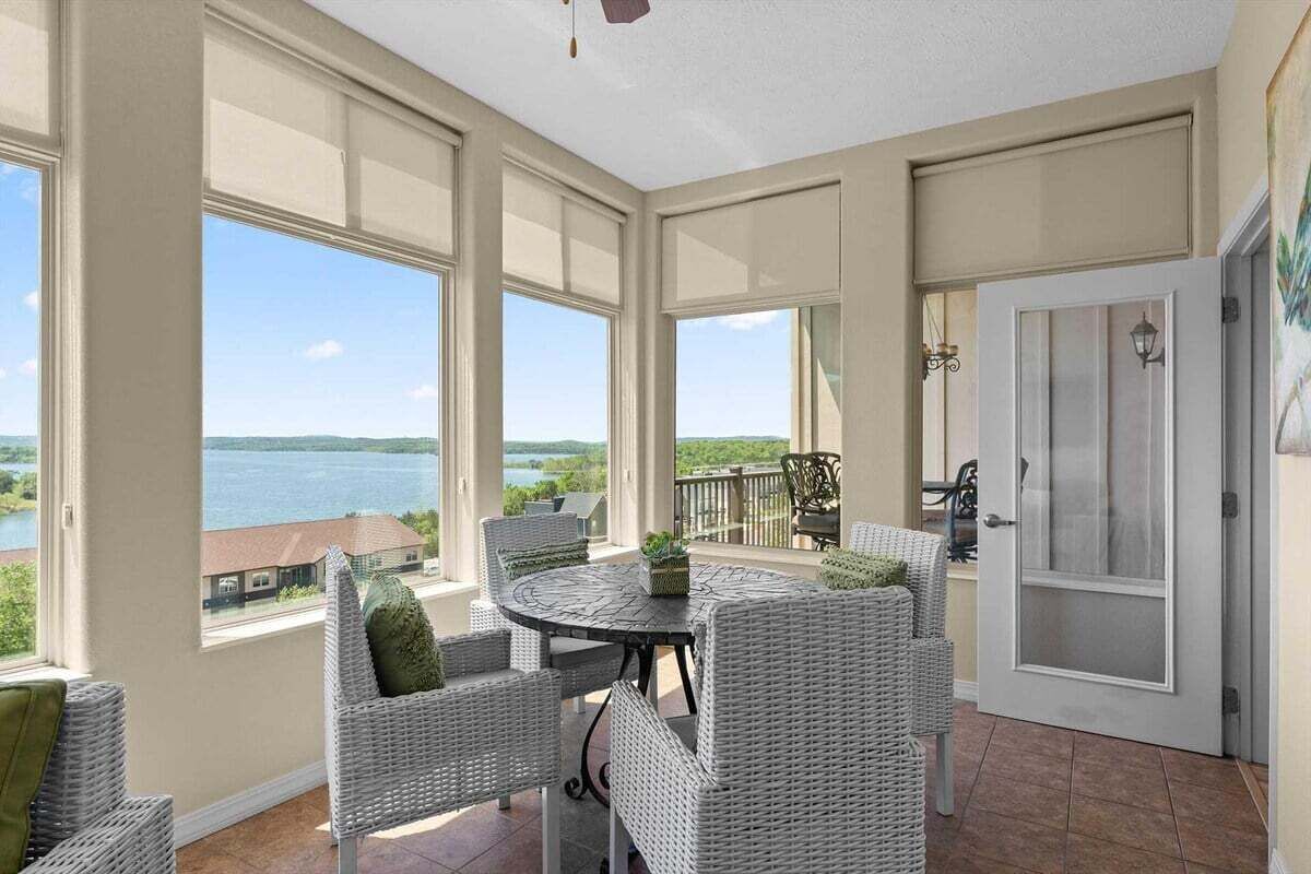 A covered patio with a view of a lake, wicker furniture, and a door with a screen.