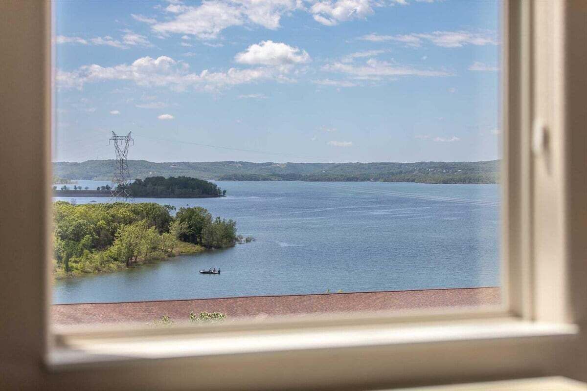 A view of a lake with a power line tower in the distance, a small boat on the water, and a forested island.
