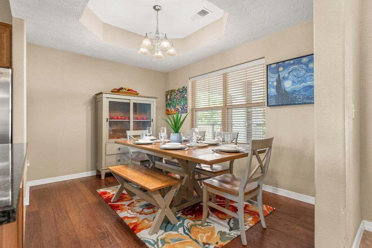 A dining area with a wooden table set for four, a cabinet with glass doors, and a painting on the wall.