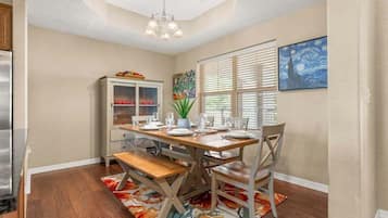 A dining area with a wooden table set for four, a cabinet with glass doors, and a painting on the wall.
