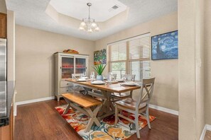 Un coin repas avec une table en bois dressée pour quatre personnes, un buffet aux portes vitrées et un tableau accroché au mur.