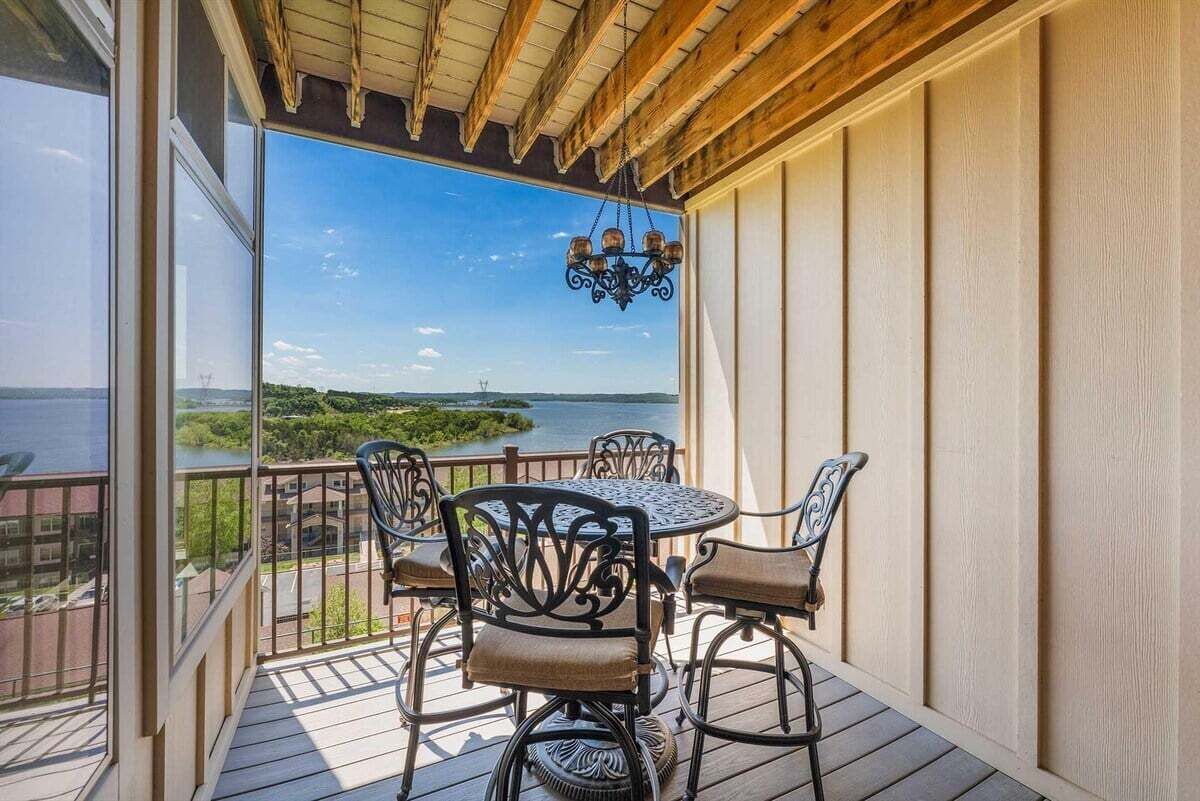 A balcony with a table and chairs, overlooking a body of water and greenery.