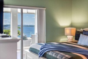 A bedroom with a bed, a nightstand, a lamp, and a view of the sea through large windows. - Luxury Majestic Condo on Table Rock Lake- Free Daily Attraction Tickets (Branson)