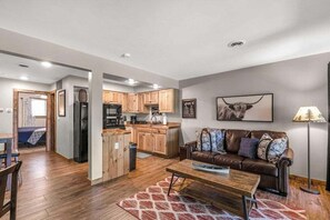 Ein modernes Wohnzimmer mit einem braunen Ledersofa, Holzböden und einer Küchenzeile mit Holzschränken und einem Kühlschrank.