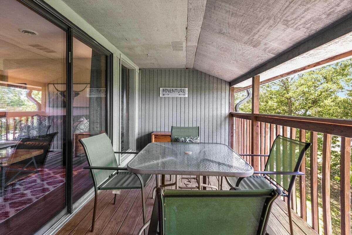 Un balcon avec une table et des chaises, une pancarte sur laquelle on peut lire « AVENTURE », et une vue sur les arbres.