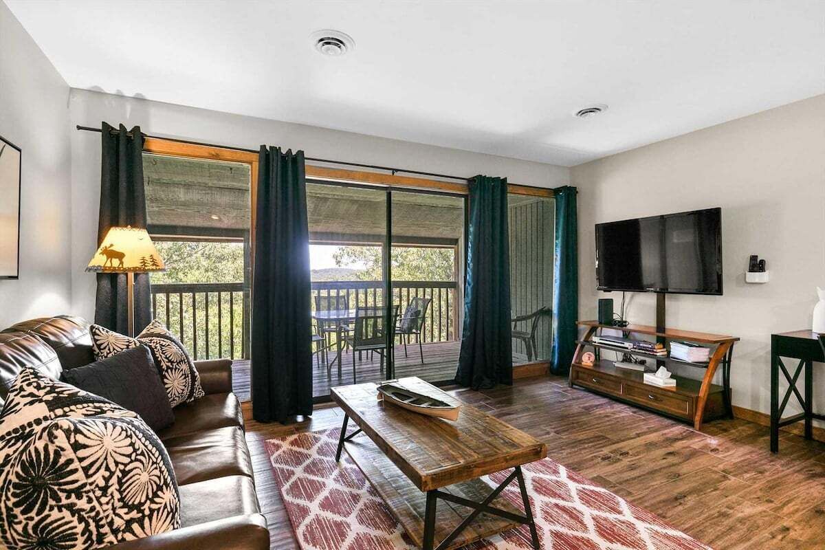 A living room with a sofa, a coffee table, a TV, and a balcony with curtains.