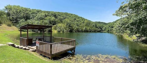 A wooden deck with a gazebo overlooking a calm river, surrounded by lush greenery.