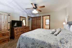 Une chambre à coucher avec un lit, une armoire en bois, un téléviseur et un ventilateur de plafond.