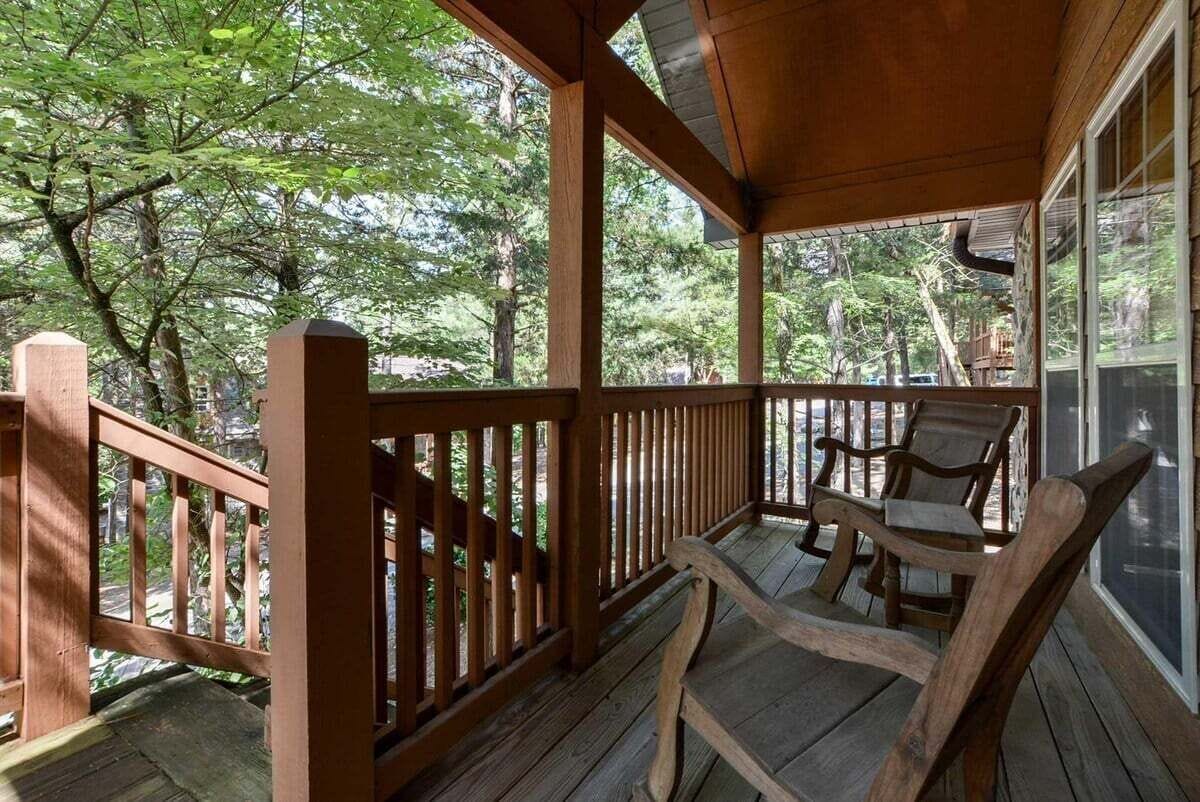 A wooden deck with a railing, a bench, and a view of a forested area.
