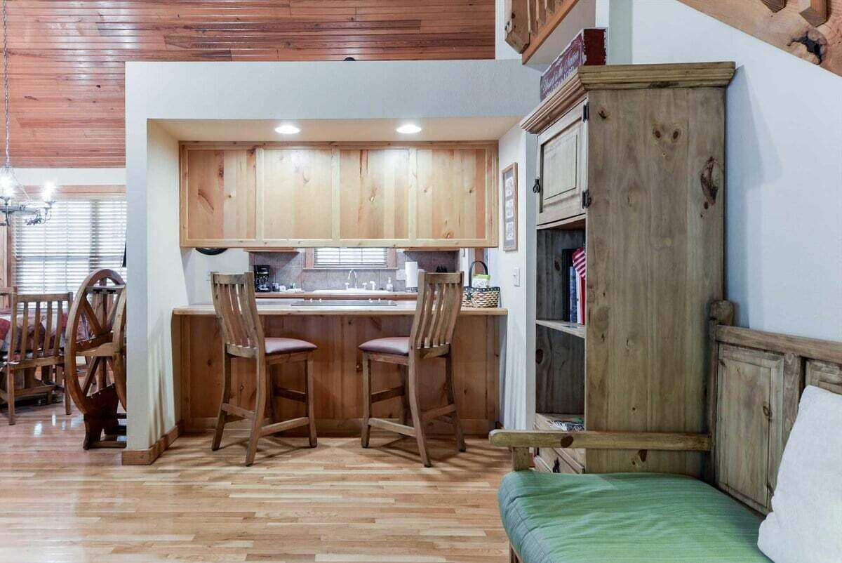 A kitchen with wooden cabinets, a bar area with stools, and a green bed in a room with wooden flooring.
