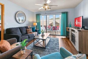 A modern living room with a sofa, coffee table, and TV. There is a balcony with a table and chairs. - Table Rock Condo_Huge Deck_New Flooring_Private_Free Tickets (Hollister)