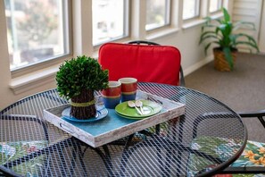 Ein runder Metalltisch mit einer Ablage, auf der sich ein Blumentopf, bunte Tassen und ein Teller mit Besteck befinden.