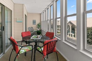 A sunlit patio with a glass table and chairs, a potted plant, and a view of a building. - Table Rock Condo_Huge Deck_New Flooring_Private_Free Tickets (Hollister)