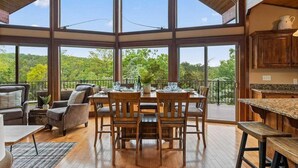 Un comedor espacioso con techo alto y ventanas grandes que dan a un paisaje exuberante.