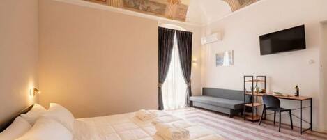 A hotel room with a bed, a desk, a chair, a television, and a window with curtains.