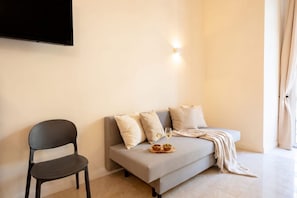 A modern living room with a sofa, a chair, a flat-screen TV mounted on the wall, and a small table with a bowl and glasses. - ALL City Hub | 6 Rooms, 9 Beds & 6 Baths in Central Bari (Bari)