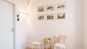A room with a white door, two white chairs, a small round table with a bowl of fruit, and six black-and-white photographs on the wall. - ALL City Hub | 6 Rooms, 9 Beds & 6 Baths in Central Bari (Bari)