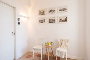 A room with a white door, two white chairs, a small round table with a bowl of fruit, and six black-and-white photographs on the wall. - ALL City Hub | 6 Rooms, 9 Beds & 6 Baths in Central Bari (Bari)