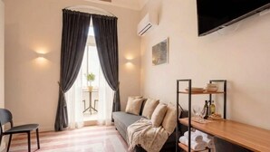 A compact living space with a sofa, a chair, a TV, a shelf with dishes, and a window with curtains. - ALL City Hub | 6 Rooms, 9 Beds & 6 Baths in Central Bari (Bari)