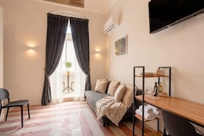 A compact living space with a sofa, a chair, a TV, a shelf with dishes, and a window with curtains. - ALL City Hub | 6 Rooms, 9 Beds & 6 Baths in Central Bari (Bari)