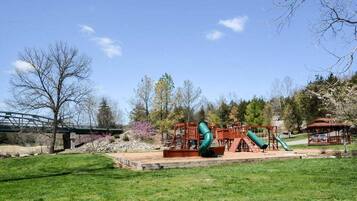 A playground with slides and swings, a bridge, and a gazebo in a park.