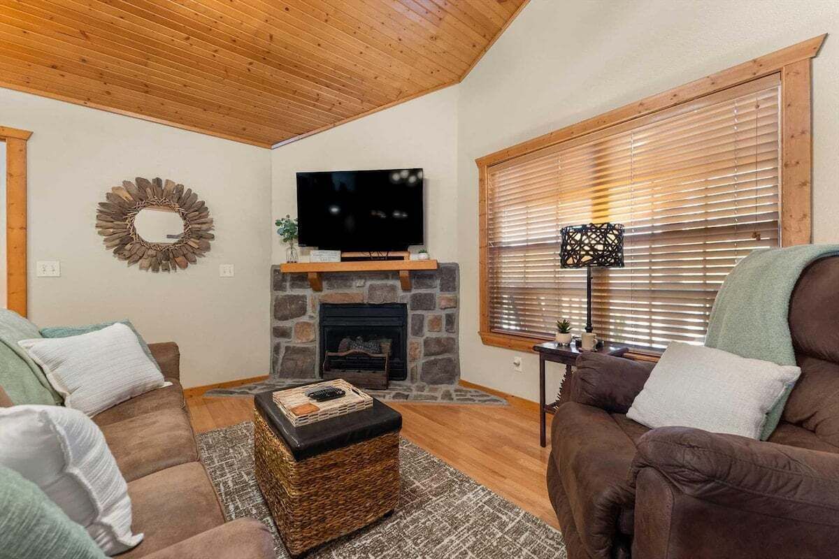A cozy living room with a stone fireplace, a flat-screen TV, and two brown sofas.