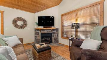 A cozy living room with a stone fireplace, a flat-screen TV, and two brown sofas.