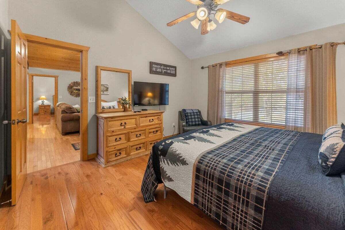 A bedroom with a bed, a television, a wooden dresser, and a ceiling fan.