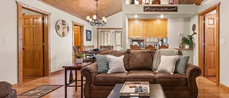 A cozy living room with a brown leather sofa, a coffee table, and a dining area with wooden cabinets.