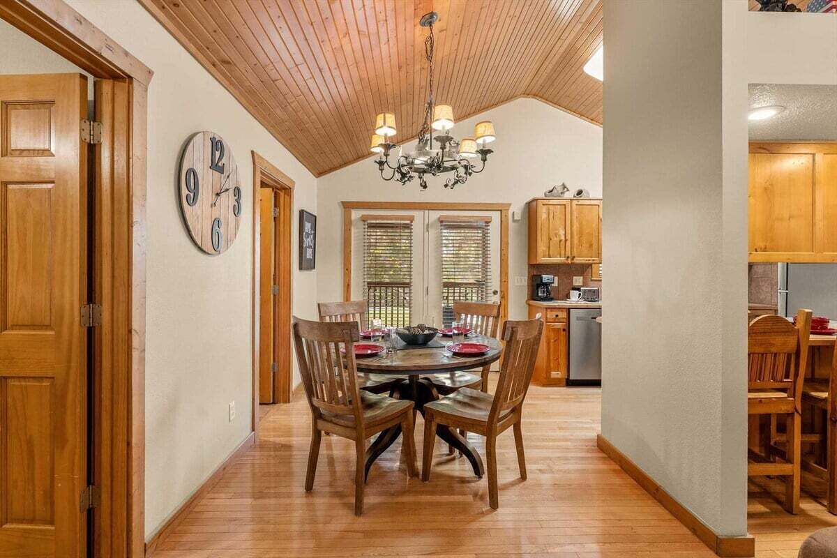 A dining area with a wooden ceiling, a chandelier, and a round table with chairs.