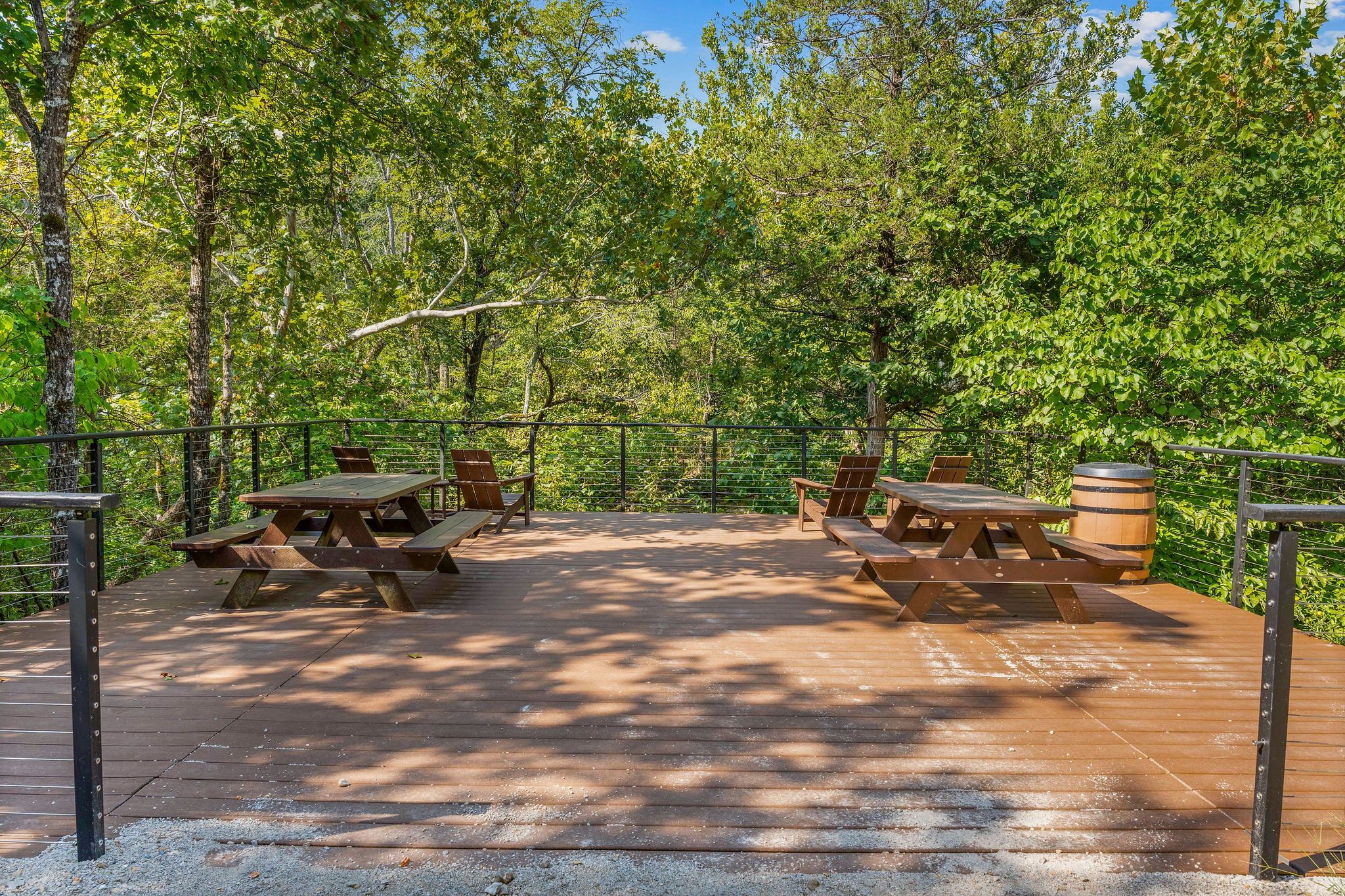 An outdoor wooden deck with picnic tables and benches, surrounded by trees.