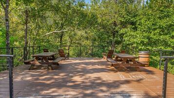 An outdoor wooden deck with picnic tables and benches, surrounded by trees.